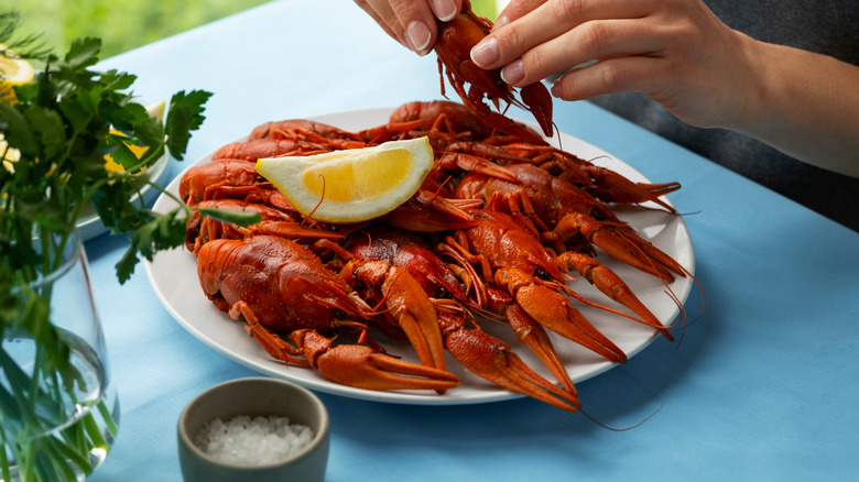 A hand peeling a crawfish over a plate of crawfish with a lemon