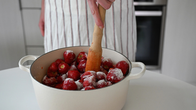 Person muddling strawberries in a pot for sweet strawberry jam