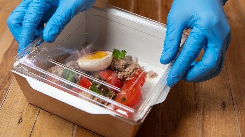 gloved hands putting lid on tuna salad container