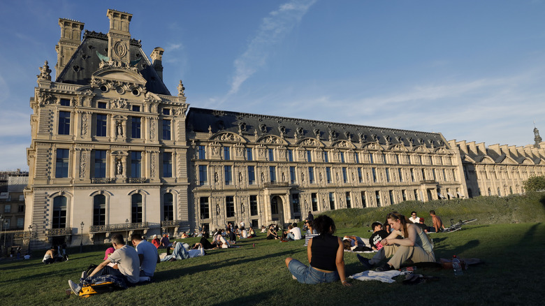 Picnickers in Paris sitting on a lawn in front of a large building