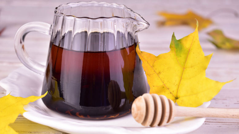 Maple syrup in glass container with autumn leaves in background