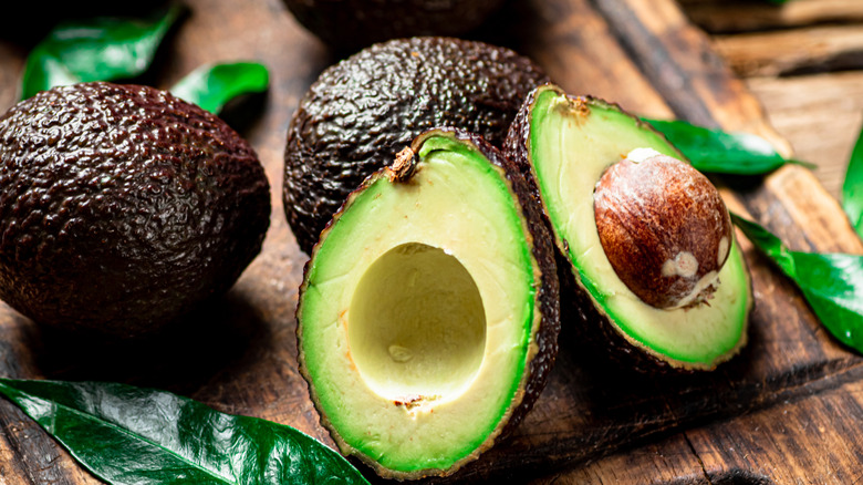 Halved avocado next to whole avocados on wood board