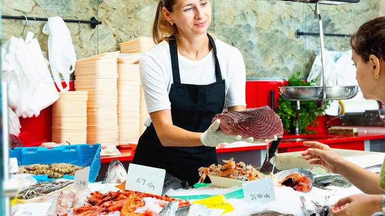 A woman showing fish to a customer at the seafood counter