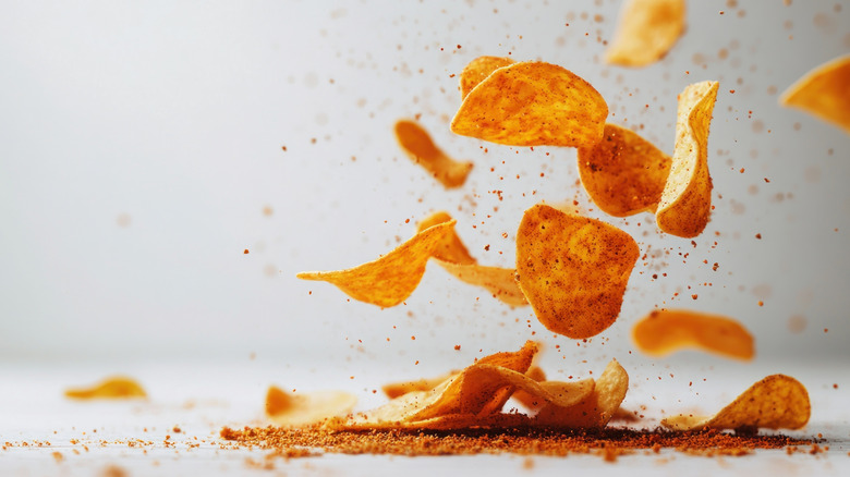 Seasoned potato chips being tossed in the air against a white background