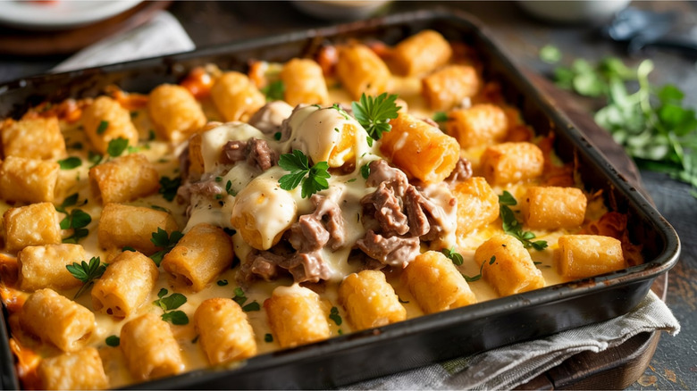 Cheesy tater tot casserole in a dish on a table with extra parsley in the background.