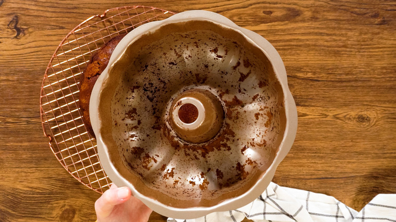 A bundt pan with cake residue stuck to the insides being held by a hand above a table