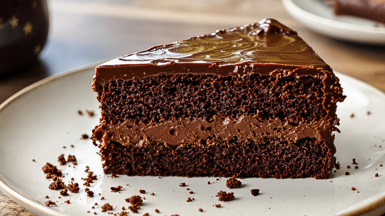 A shiny slice of chocolate cake on a white plate