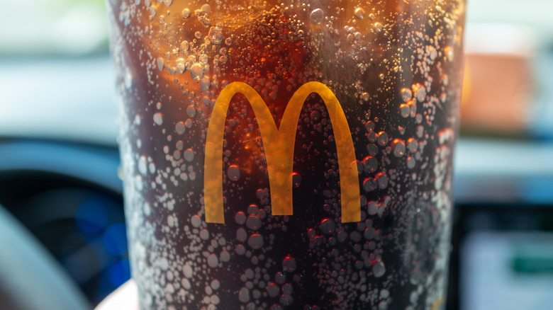 Close up of of the McDonald's logo on a clear cup with brown soda and carbonation bubbles on the side.